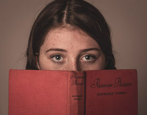 Photograph of girl's eyes shown peeking over an open book
